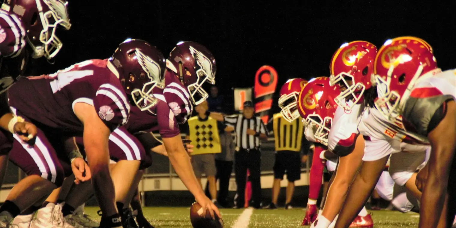 Two college football teams lined up at the line of scrimmage under the lights