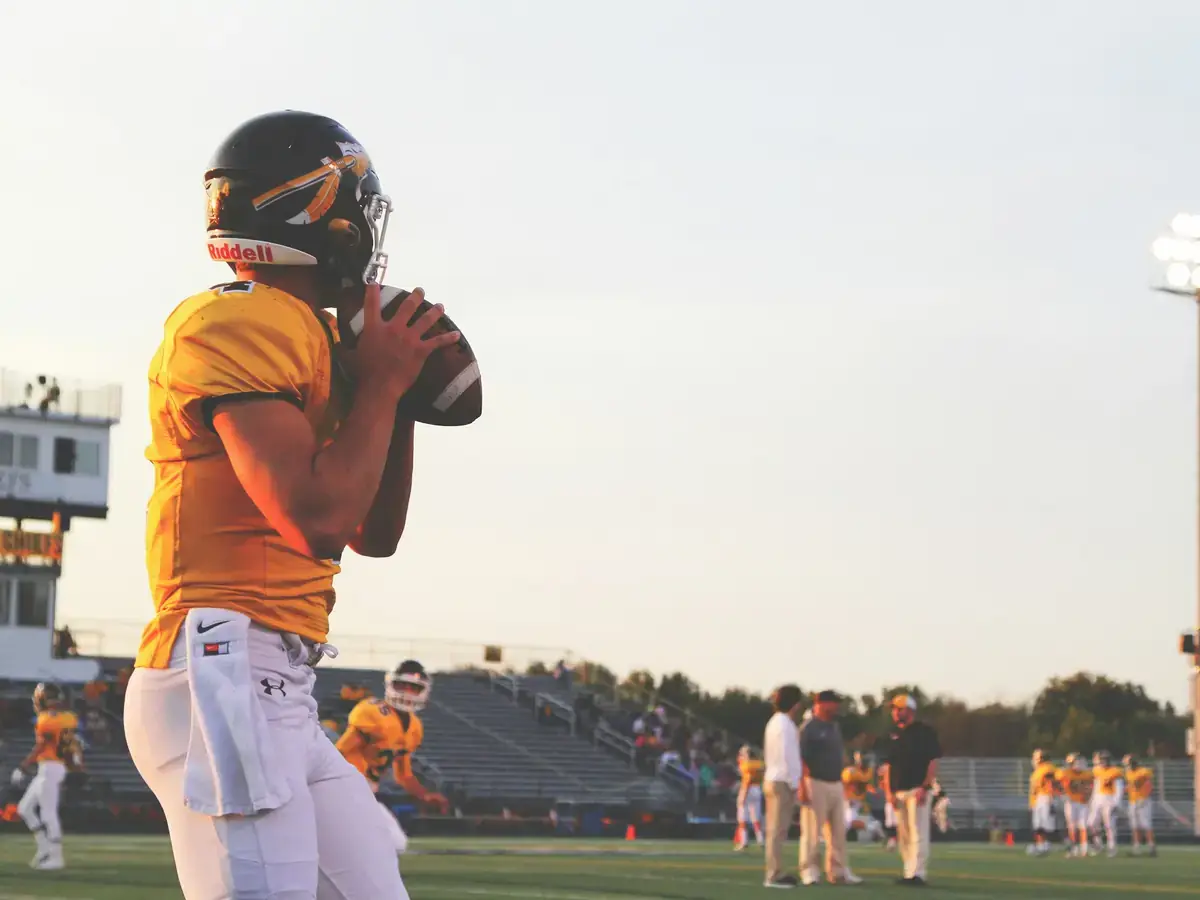 Quarterback in a gold jersey setting up to throw at sunset