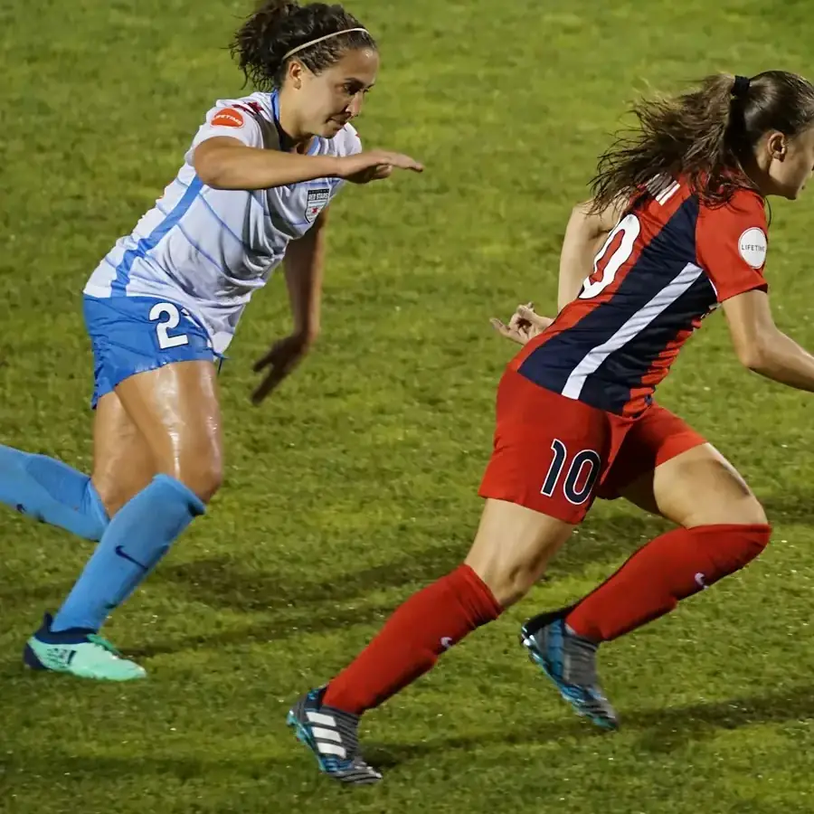 Two women's soccer players racing for the ball at night