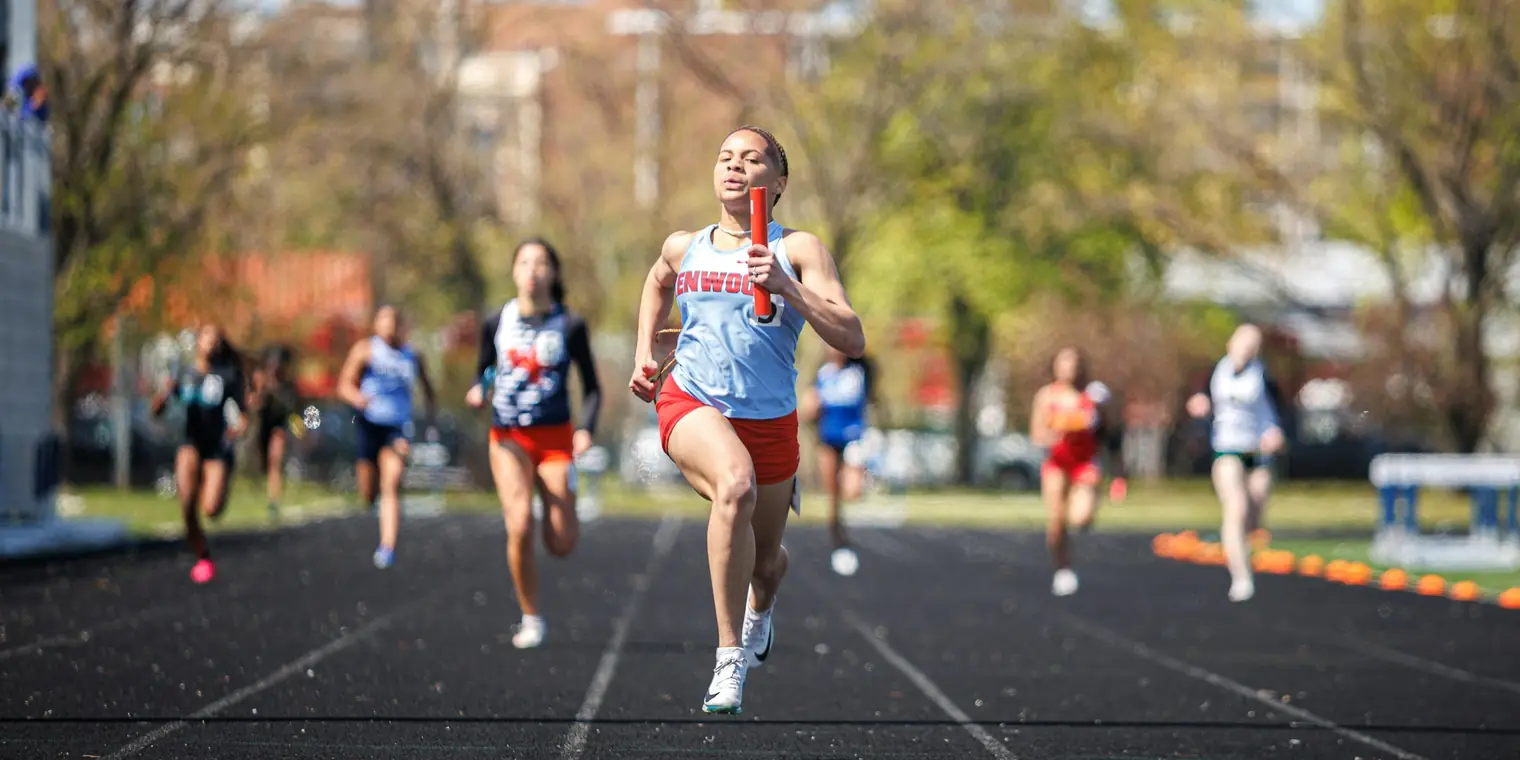 A high school sprinter carrying a relay baton down the home straight ahead of the field
