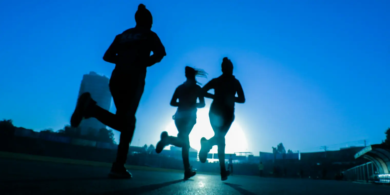 Three athletes running on a track in silhouette against a bright blue morning sky